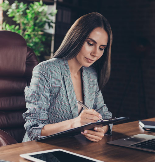 Attractive professional woman signing paperwork on a clip board whilst sitting at her desk