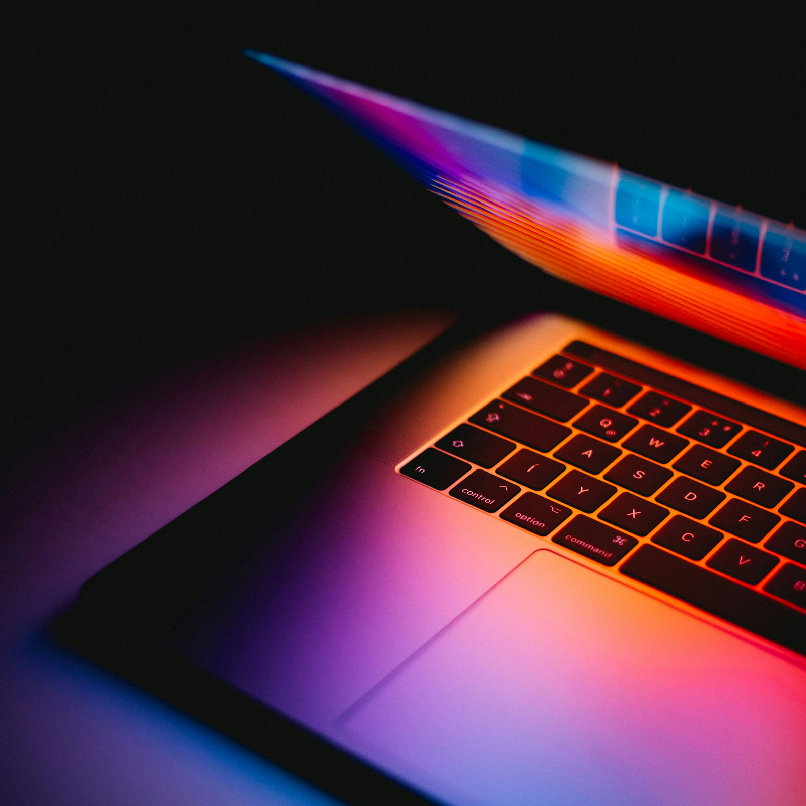 A partially open laptop emits vibrant, colorful light from its screen, illuminating the keyboard in shades of pink, orange, and blue. The background is dark, emphasizing the luminous glow from the device—a brilliant symbol for innovative law firm marketing services.