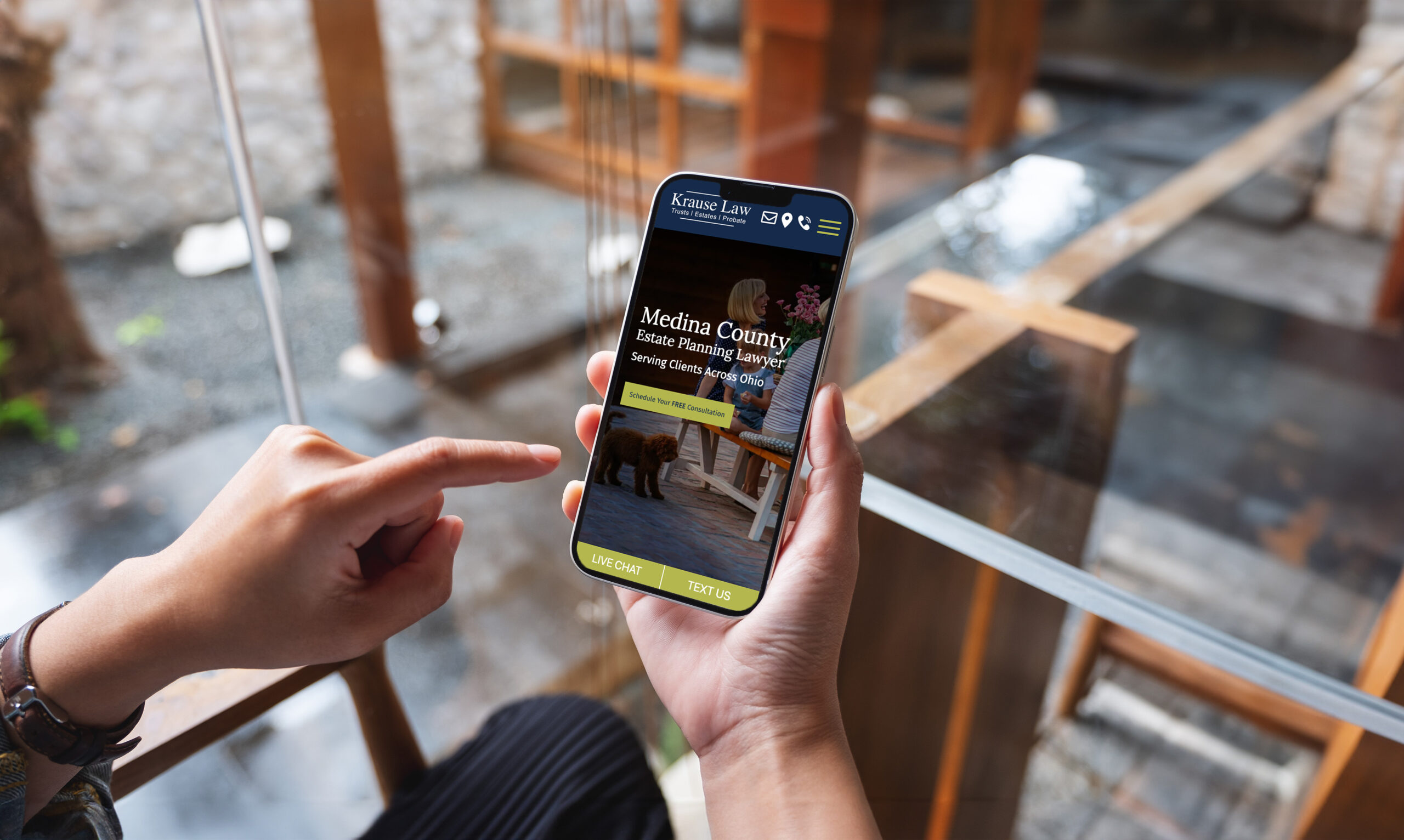 A person holding a smartphone, with their finger pointing to the screen. The phone displays a law firm's website with the header 