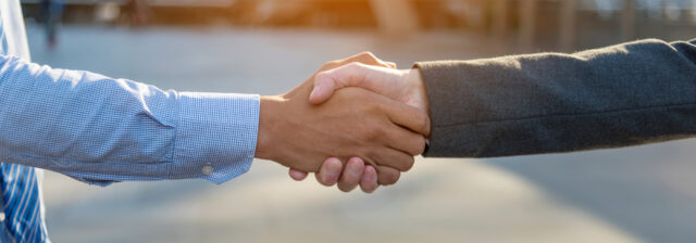 2 men in business shirts shaking hands in warm outdoor late afternoon lighting - Reputation Management concept image