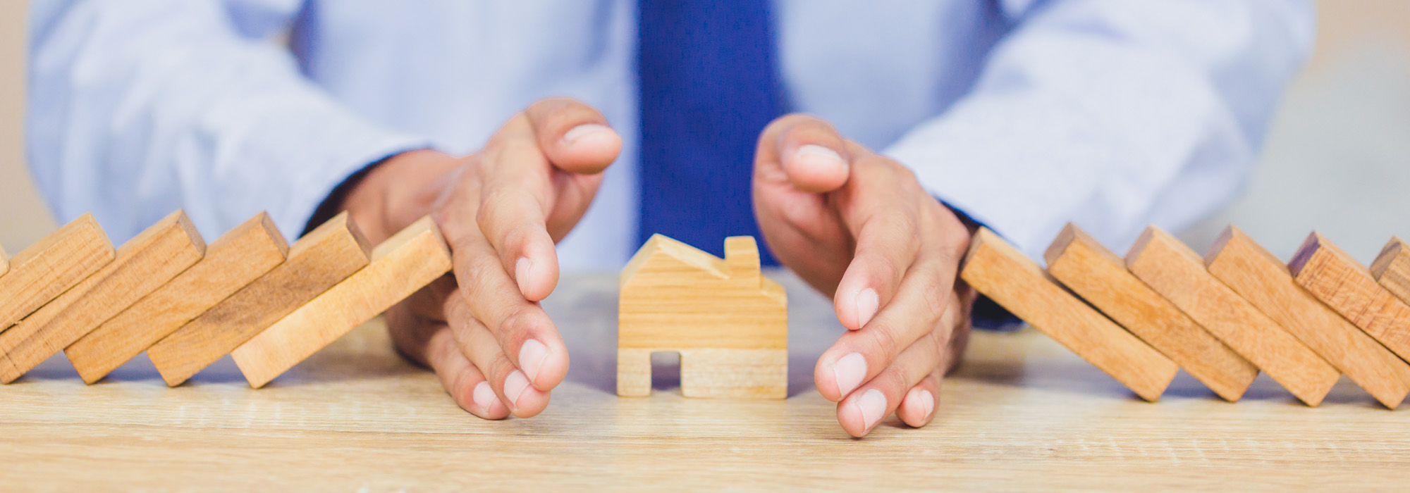 Businessman hand stopping risk the wooden blocks from falling on house