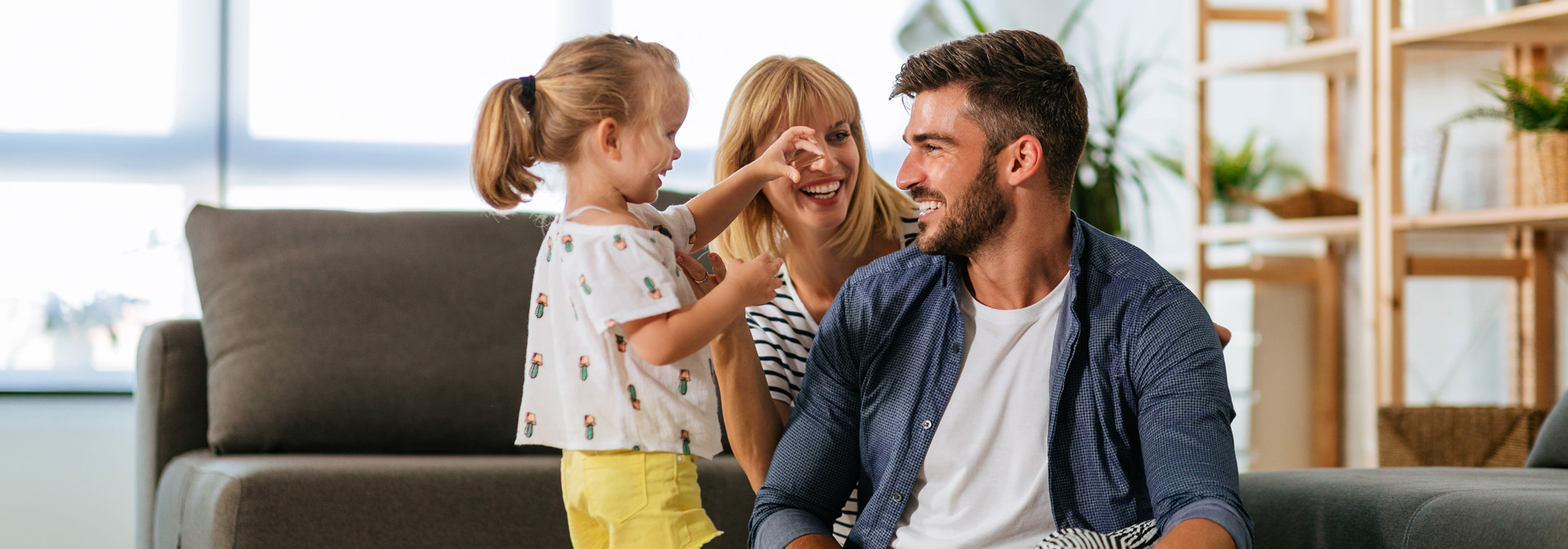 Young cheerful parents playing on floor with young daughter at home