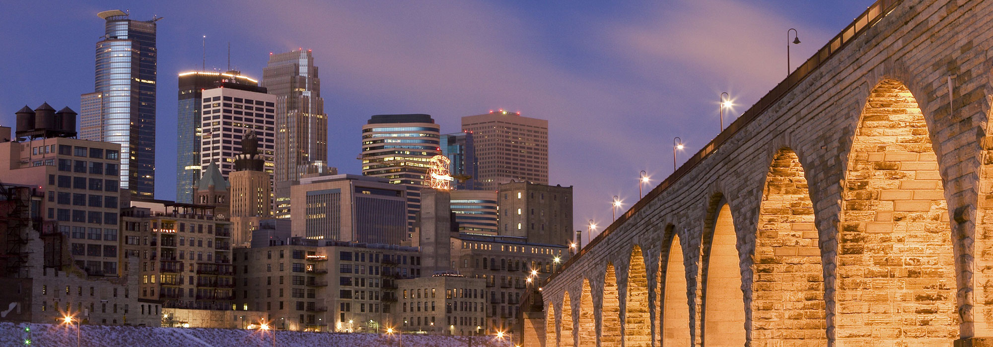 Minneapolis, Minnesota lit up behind Stone Arch Bridge at dusk