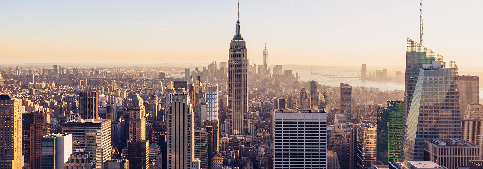 A panoramic view of New York City at sunset, featuring a skyline with iconic skyscrapers including the Empire State Building at the center, surrounded by other high-rise buildings. The sky is clear with a warm, golden hue reflecting off the buildings, reminiscent of excellence in law firm marketing services.