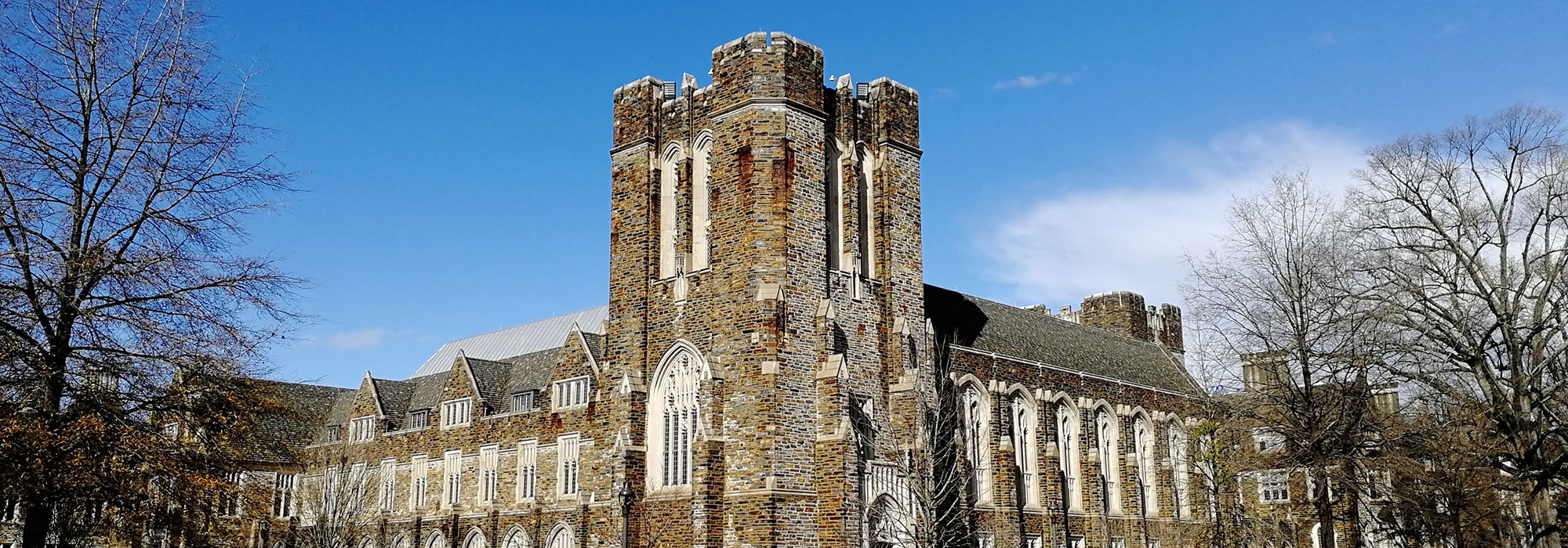A historic building with a tall, crenelated stone tower stands under a clear blue sky. The structure features arched windows and is surrounded by bare trees. North Carolina Law Firm Marketing concept image