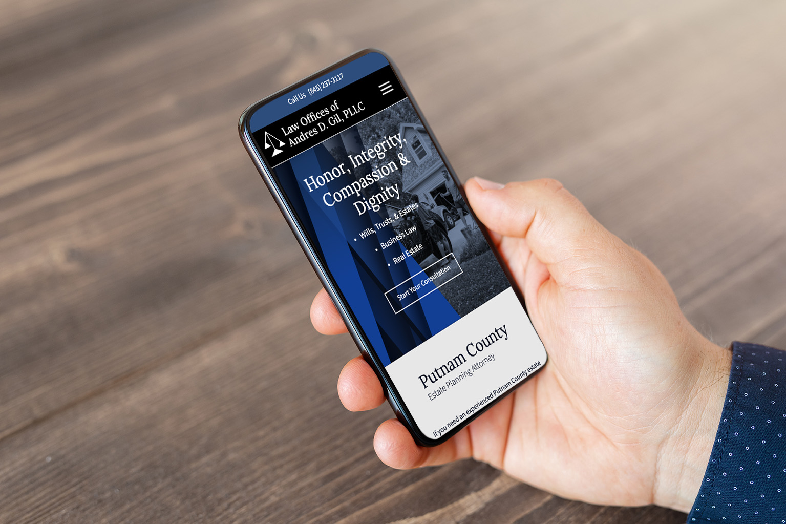 A hand holding a smartphone displaying a law firm website. The screen shows contact information, the firm’s values 