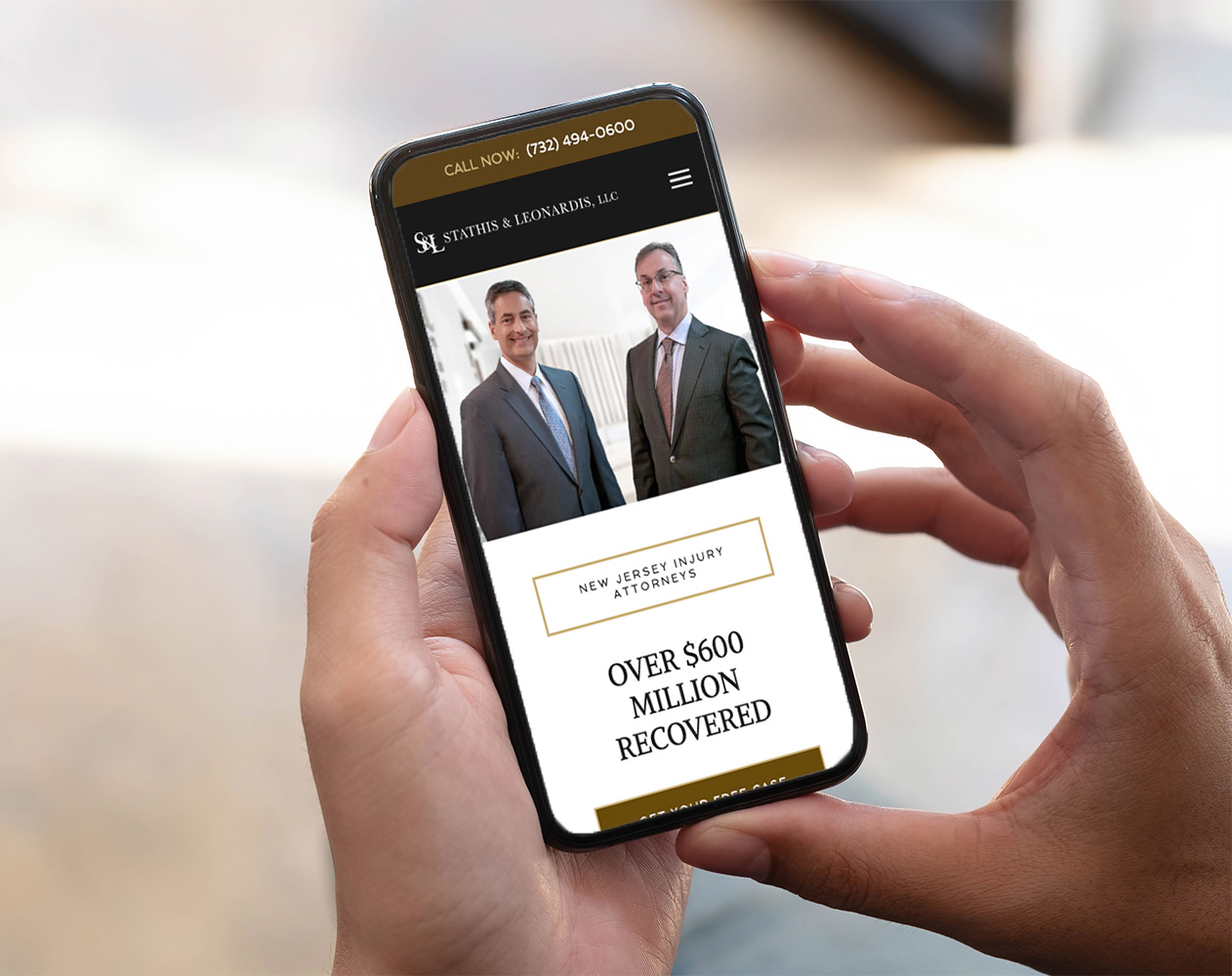 A person holding a smartphone displaying a website for a law firm, featuring two men in suits and text about New Jersey injury attorneys. The screen highlights over $600 million recovered for clients.