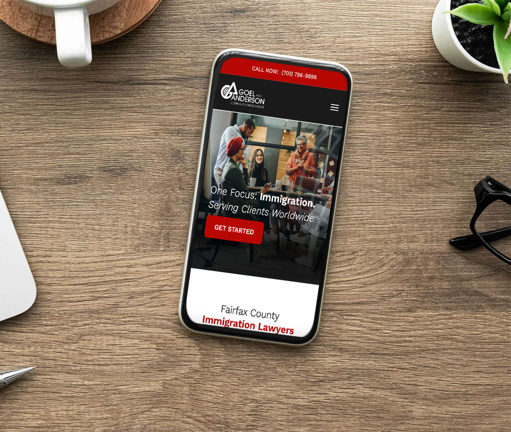 A smartphone on a wooden desk displays a website for Gogel & Anderson Immigration Lawyers, featuring a group photo, a 