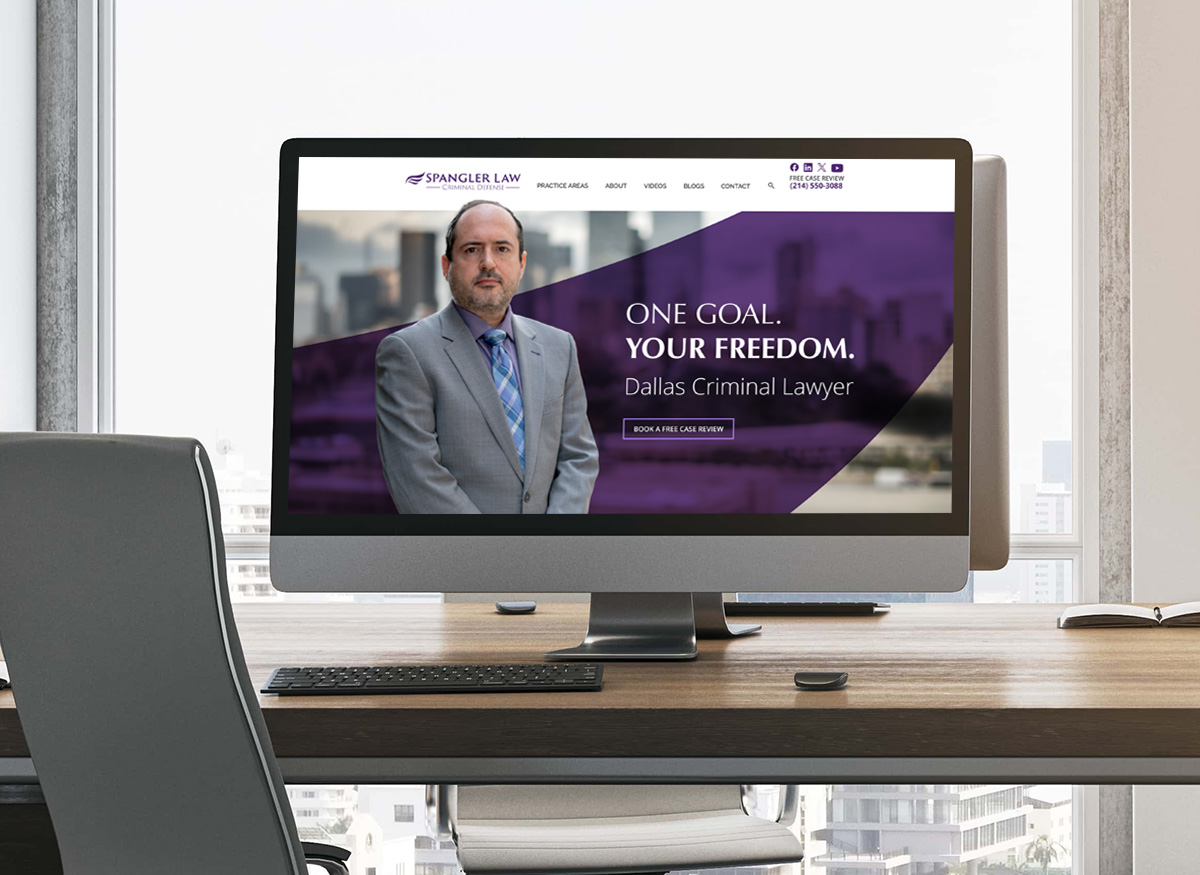 A desktop computer on a modern office desk displays a law firm's website featuring a man in a suit and text that reads