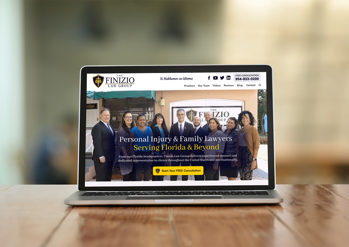 A laptop on a wooden table displays The Finizio Law Group website, showing a group of seven professionally dressed people standing together and promoting personal injury and family law services.