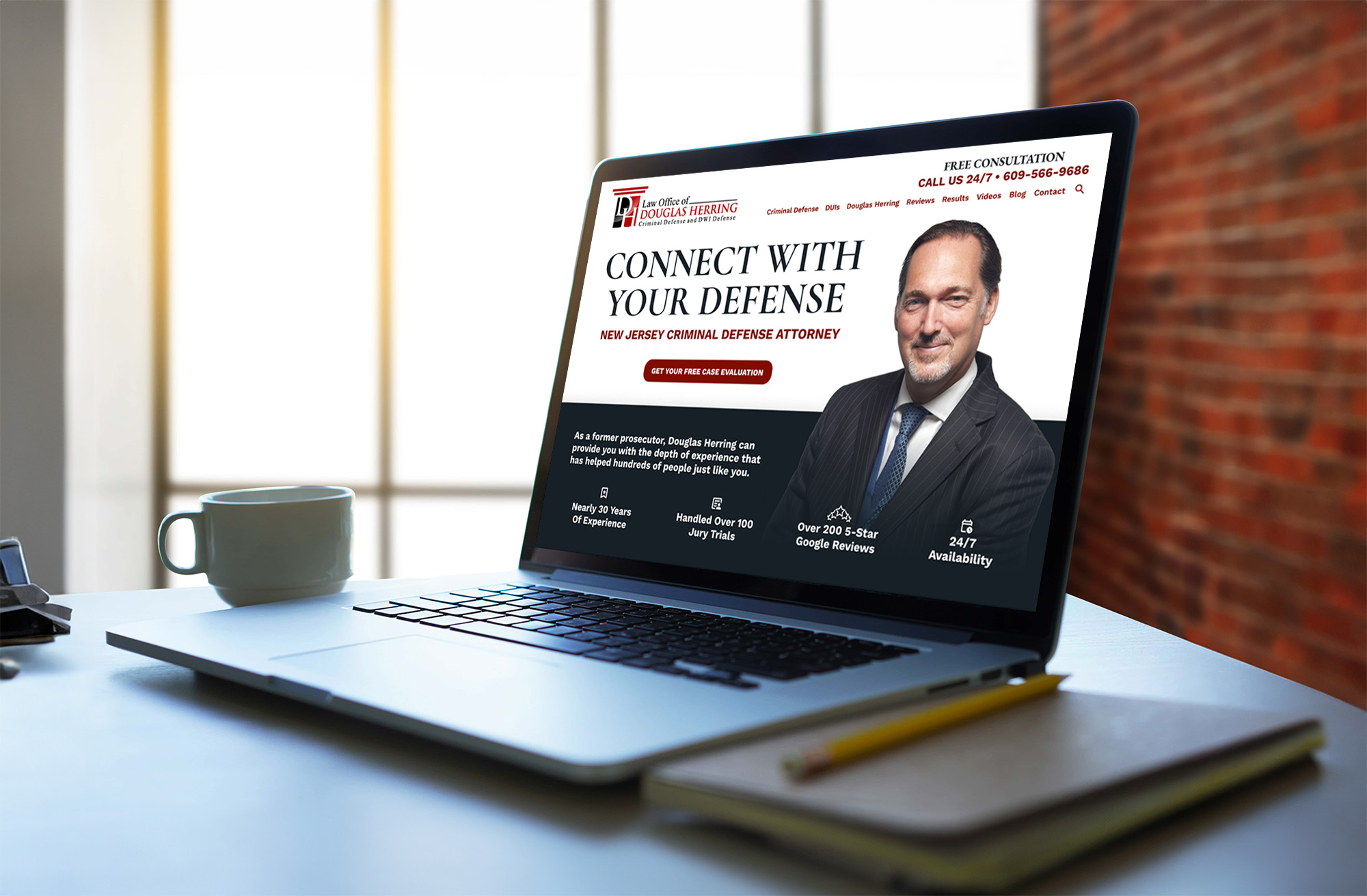 A laptop on a desk displays a website for a New Jersey criminal defense attorney, featuring a suited man, contact info, and a call for a free consultation. A cup, mobile phone, and notebook are beside the laptop.