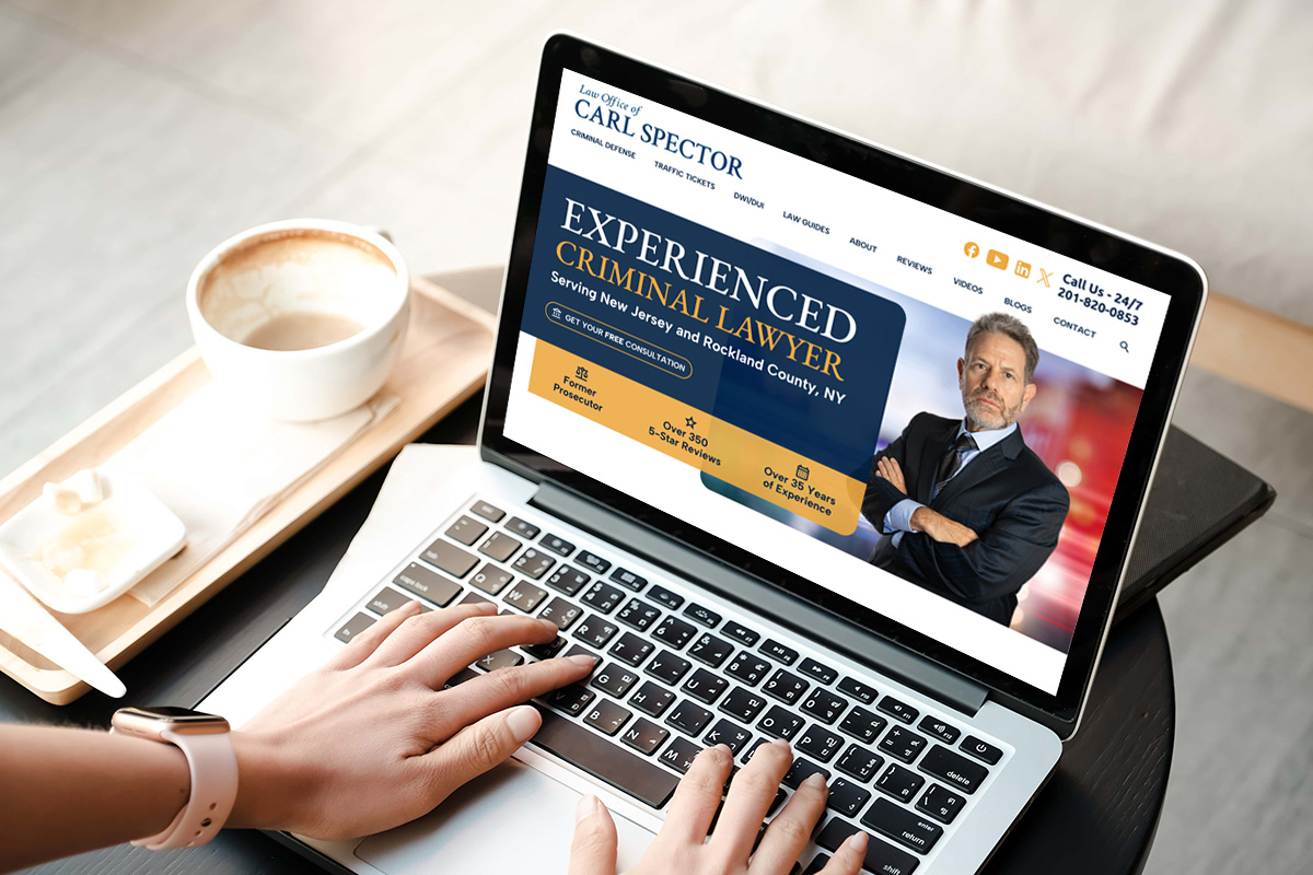 A person types on a laptop displaying a website for an experienced criminal lawyer. Next to the laptop is a cup of coffee on a saucer and a notepad with a pen on a wooden tray.