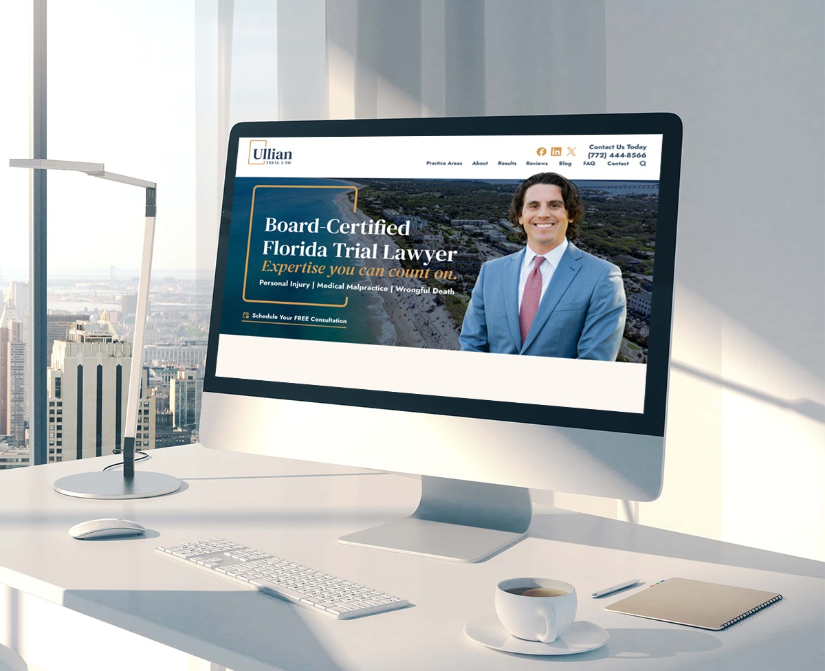 A computer screen on a bright office desk displays a law firm's website featuring a man in a suit smiling, with text promoting a board-certified Florida trial lawyer. City buildings are visible through large windows in the background.